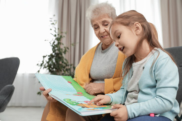Obraz premium Cute girl and her grandmother reading book at home