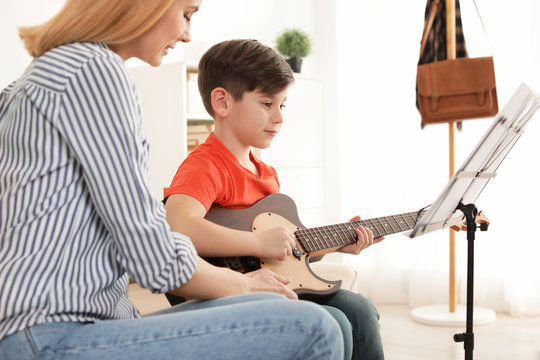 Little boy playing guitar with his teacher at music lesson. Learning notes - Powered by Adobe
