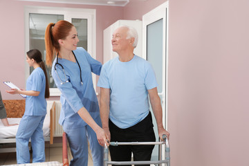 Nurse assisting senior patient with walker in hospital ward