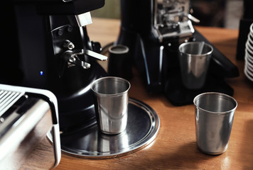Metal cups near coffee grinding machine on wooden table