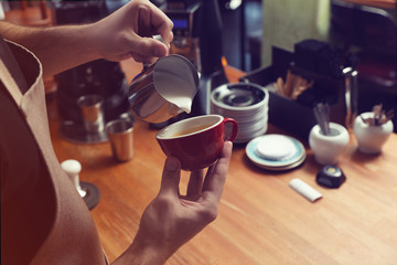 Barista pouring milk into coffee cup at bar counter, closeup. Space for text