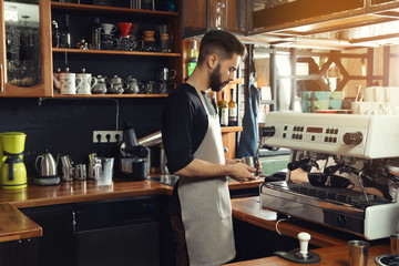 Barista frothing milk in metal pitcher with coffee machine steam wand at bar counter