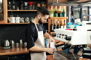 Barista pouring milk into metal jug near coffee machine at bar