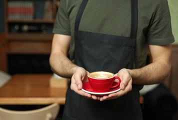 Barista with cup of coffee in shop, closeup. Space for text
