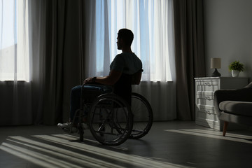 Young man sitting in wheelchair near window indoors