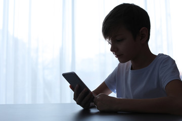 Child with smartphone at table indoors. Danger of internet