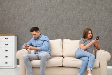 Couple engaged in smartphones while spending time together at home. Loneliness concept
