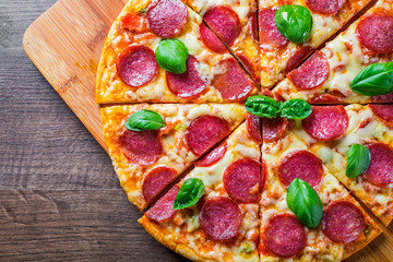 Pepperoni Pizza with Mozzarella cheese, salami, Tomato sauce, pepper, Spices and Fresh basil. Italian pizza on wooden table background