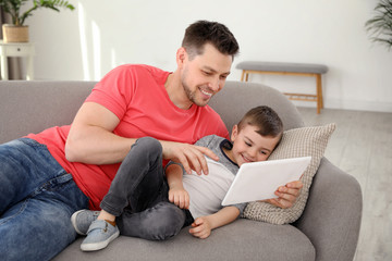 Boy and his father with tablet lying on sofa at home. Family time