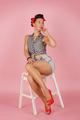 Beautiful young bright girl in retro style pin-up style, sits on a white step ladder on a pink glamorous background