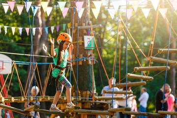 Adorable little girl enjoying her time in climbing adventure park on warm and sunny summer day....