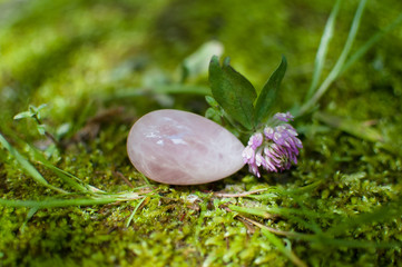 Rose quartz crystal vaginal yoni egg lying on the green grass during sunny summer day. Female health concept