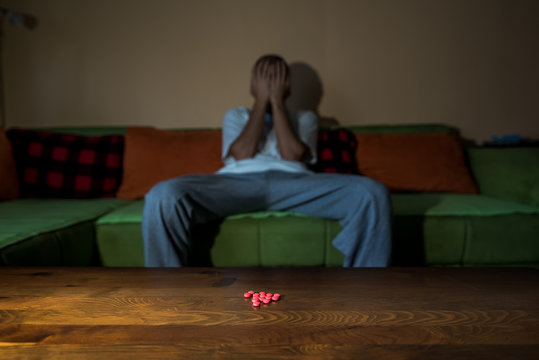 Depressed man suffering from suicidal depression want to commit suicide by taking strong medicament drugs and pills pain killers while he sitting in his dark room selective focus moody dramatic look