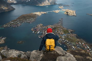 Man sitting on cliff edge alone enjoying aerial view backpacking lifestyle travel adventure outdoor vacations in Norway top of Reinebringen mountain.