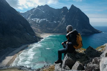 Poster Man sitting on cliff edge alone enjoying aerial view backpacking lifestyle travel adventure outdoor vacations in Norway top of Reinebringen mountain. © puzurin