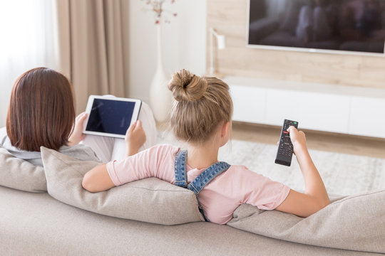 Mother And Daughter Sitting On Couch Watching Tv In Living Room