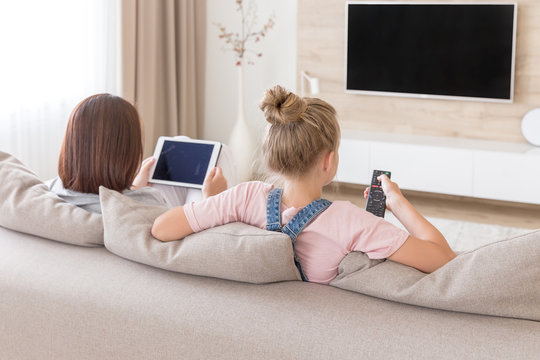 Mother And Daughter Sitting On Couch Watching Tv In Living Room