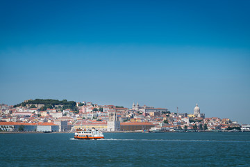 Obraz premium A traditional ferry boat (Cacilheiro) crossing the Tagus River with the Lisbon skyline on the background.