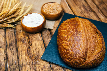 Baked fresh rye, loaf or whole grain brown bread, wheat ear or spike and flour  on wooden board table. Bakery concept image.
