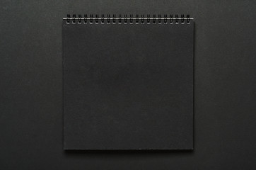 Black notebook on a spiral on a black background. Copy space, top view, flat lay, mock up.