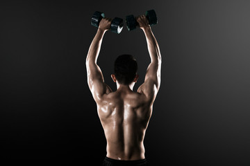 Fototapeta na wymiar Back view of muscled man lifting dumbbells