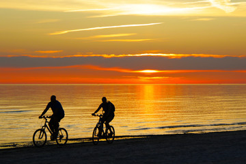 Obraz na płótnie Canvas couple riding a bicycles and sunset over the sea on background
