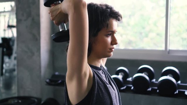 Young Caucasian fit woman doing overhead triceps extension exercise with dumbbell at the gym