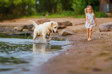 Little girl playing with labrador dog, near lake