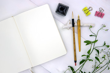 Blank page of sketchbook with calligraphy tool. Notebook top view photo on white background. Spring or summer flat lay