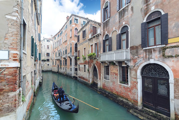 Fototapeta na wymiar Gondolier punting gondola through green canal in Venice.