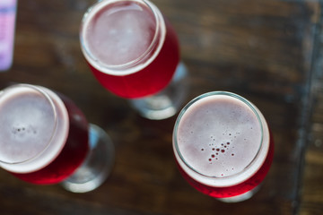 Three glasses with red wine on a wooden table. Glasses of cherry beer are on the table. There is no one in the frame.