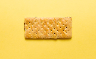 Top view of one buttery cracker with holes and salt on yellow background