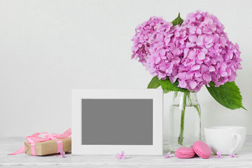 Modern still life with pink hydrangea flowers, photo frame, coffee cup and gift box on white wooden table