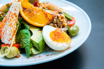 Healthy vegetables green caesar or greek mediterranean salad with boiled egg and fruits in white porcelain dish on table for vegetarian on black background from top view.