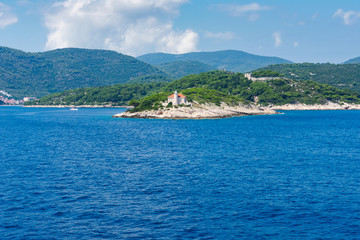 Seascape view of a small lighthouse on a green peninsula at the entrance of city of Vis harbour in Croatia, on a bright summer day