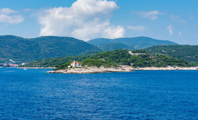 Seascape view of a small lighthouse on a green peninsula at the entrance of city of Vis harbour in Croatia, on a bright summer day