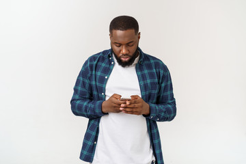 Smiling black young man in glasses holding phone looking at smartphone isolated on white grey studio background.