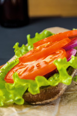 Breakfast tomato sandwich with salad on black wood background.