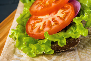 Breakfast tomato sandwich with salad on black wood background.