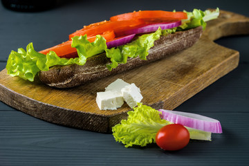 Breakfast tomato sandwich with salad on black wood background.