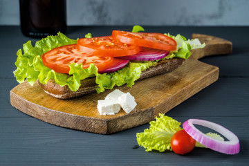 Breakfast tomato sandwich with salad on black wood background.