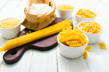 uncooked pasta variations and flour in paper bag, on white wooden table