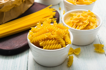 uncooked pasta variations and flour in paper bag, on white wooden table