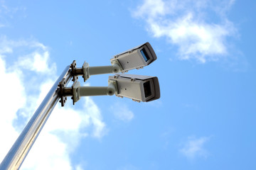 Surveillance cameras seen from below with sky background.