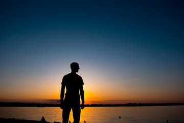 The young man is standing before the river bank with yesllow - blue Sunrise or sunset
