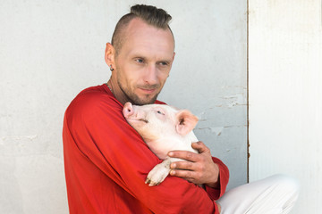 Pig farmer with cute piglet in hands at farm wall. Focus on piggy.