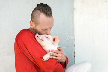 Pig farmer with cute piglet in hands at farm wall. Focus on piggy. © bohemama