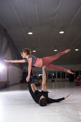 Young couple practicing akroyoga on a mat in the gym together. Woman flies. Man and woman sport training acrobatics yoga inside. Affiliate yoga, flexibility, trust concept. Teamwork