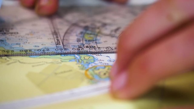 A ships captain using a protractor on a nautical chart while on a rolling sea, close up