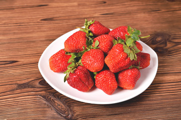 red large strawberries in a white plate on a natural brown background